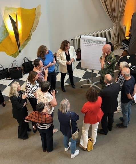 groep mensen staat in een zaal in een kring voor een witte flipover met een miniltair ernaast