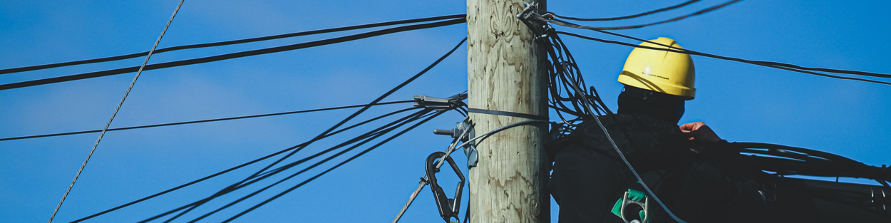 foto van een man werkend aan een telefoonpaal met kabels - ter illustratie van Agentschap Telecom