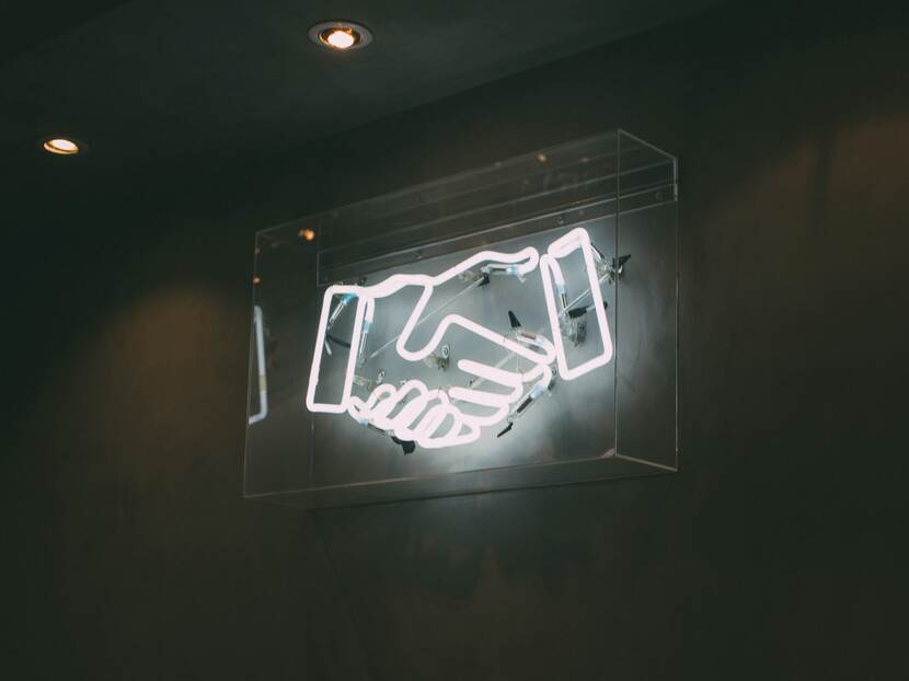 foto van een neon bord met schuddende handen