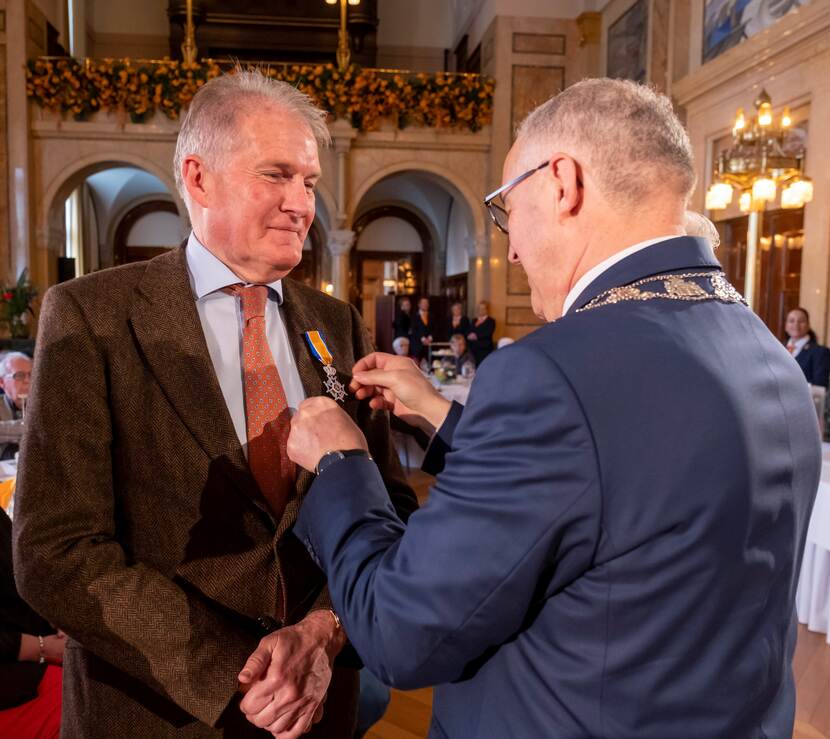 Jan van den Bos krijgt zijn onderscheiding opgespeld door burgemeester Aboutaleb