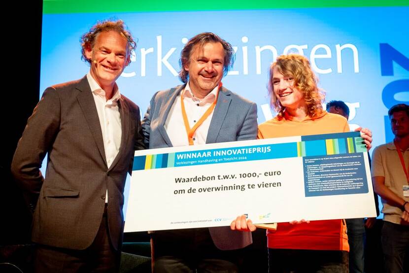 Projectleider DiTeCT Wilfred Mijnheer van Inspectie Gezondheidszorg en Jeugd neemt samen met zijn zoon de juryprijs in ontvangst van juryvoorzitter Mark Bressers: een bronzen beeld van Corry Ammerlaan en een cheque van € 1000,- om de winst te vieren met de projectleden.