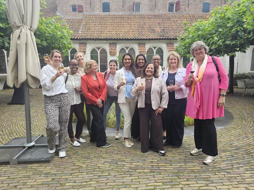 Groepje van 11 vrouwen staat voor een oud pand en heffen vrolijk een glas recht de camera inkijkend