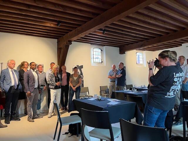 vrouw neemt een foto van een tiental mensen staand onder een donker houten plafond