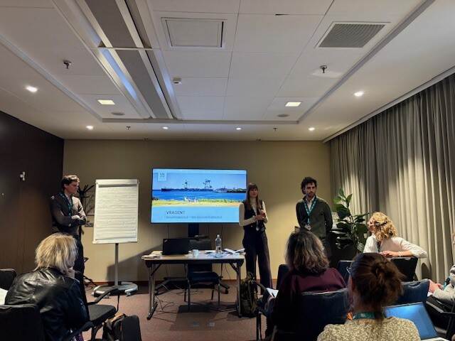 3 mensen staan voor een zaaltje met een beeldscherm en een flipover