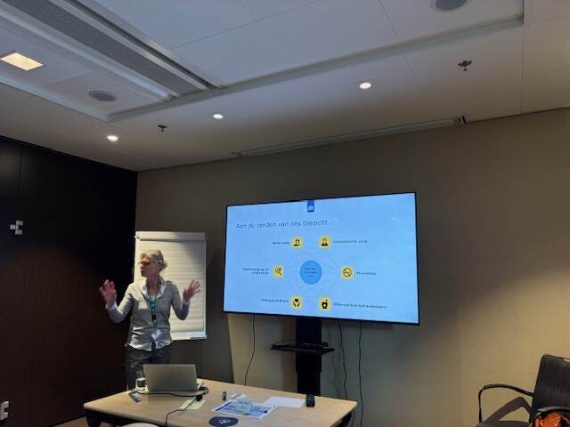 Vrouw staat met handen omhoog voor een beeldscherm wat uit te leggen