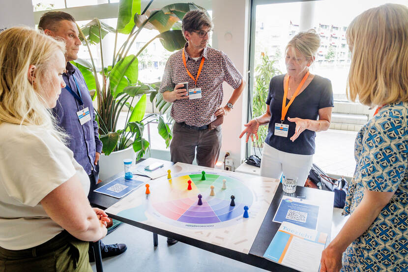 Vijf mensen staan rond tafel met daarop een bordspel