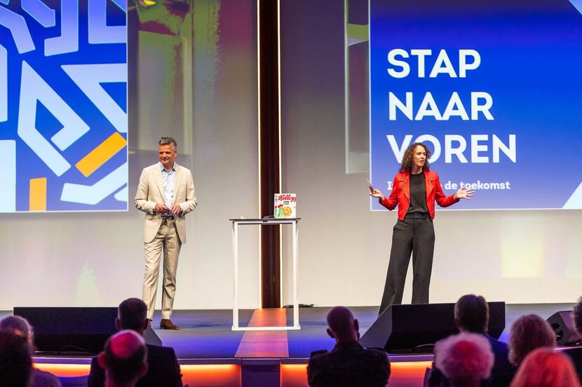 man en vrouw op podium voor een groot beeldscherm