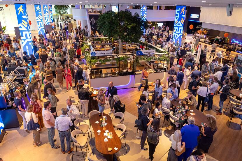 Overzichtsfoto van bovenaf van een zaal waarin mensen met elkaar praten bij standjes