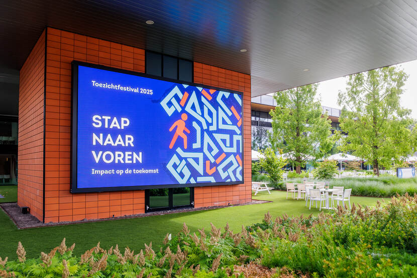 Op een groot blauw beeldscherm tussen het groen staat de tekst stap naar voren met een tekening erbij