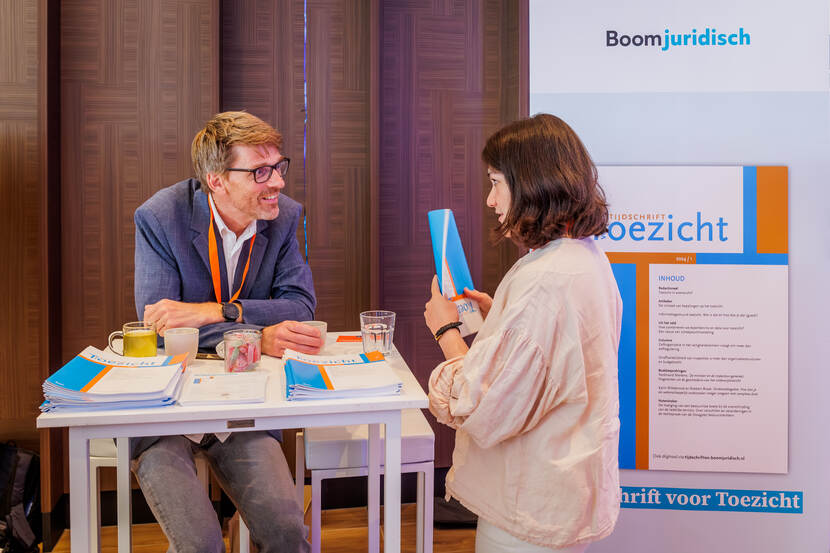 man zittend achter tafel in gesprek met vrouw over een tijdschrift