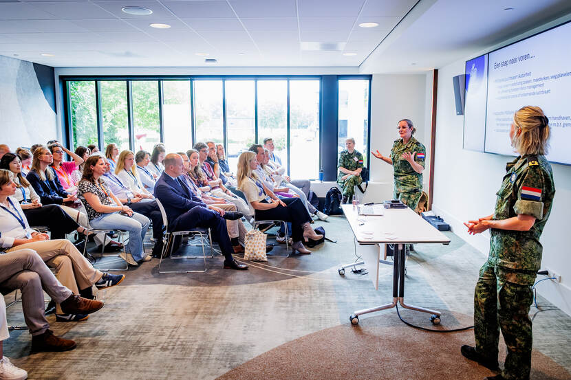 Drie vrouwelijke militairen staan voor een zaaltje met zittende mensen
