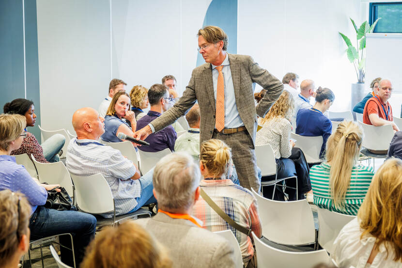 Man met microfoon stelt vraag aan andere man in een zaaltje