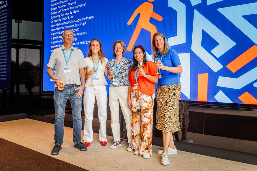 1 man en 4 vrouwen staan voor blauw gekleurd beeldscherm,